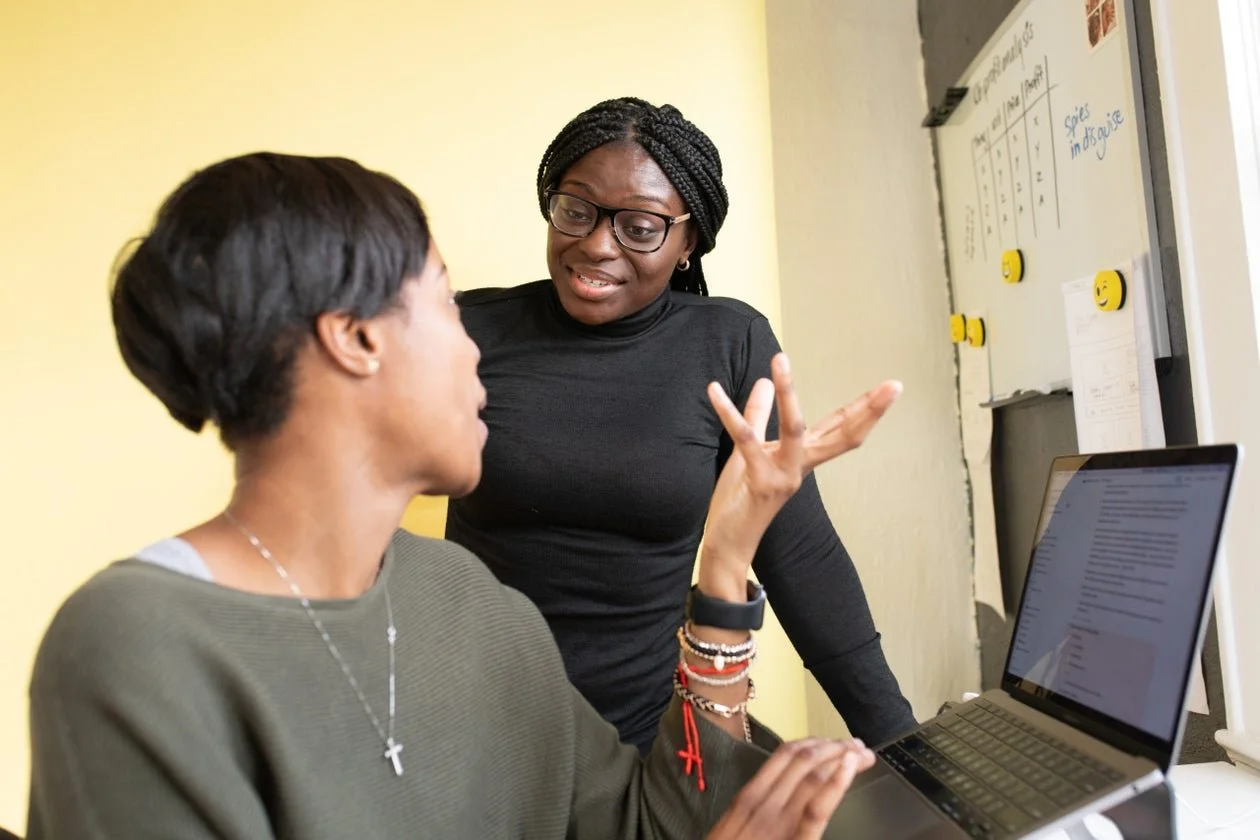 Two African women collaborating beside a laptop and whiteboard