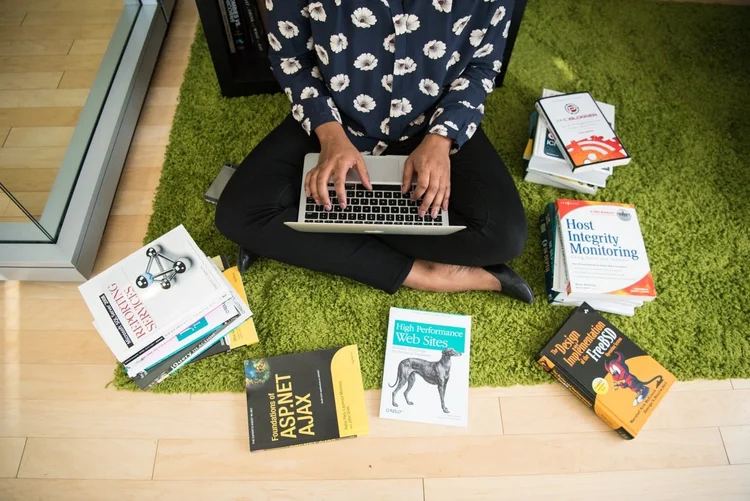 A person working on a laptop surrounded by books